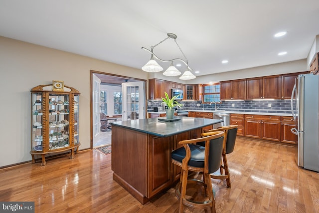 kitchen with a kitchen bar, stainless steel appliances, light hardwood / wood-style flooring, a kitchen island, and hanging light fixtures