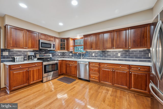 kitchen with appliances with stainless steel finishes, light wood-type flooring, backsplash, and sink