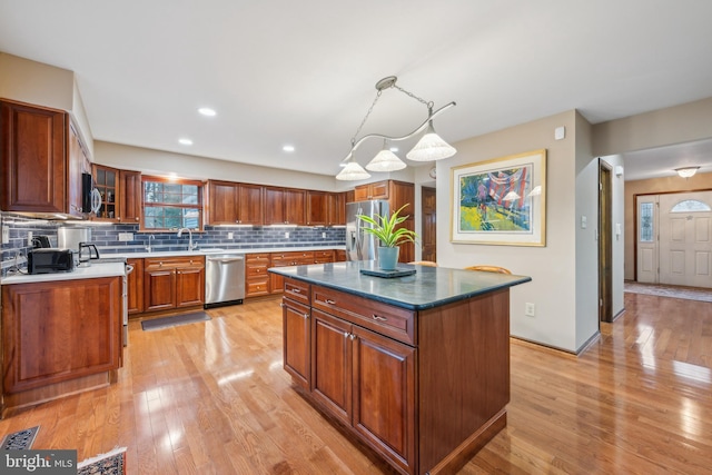 kitchen featuring hanging light fixtures, light hardwood / wood-style flooring, tasteful backsplash, a kitchen island, and stainless steel appliances