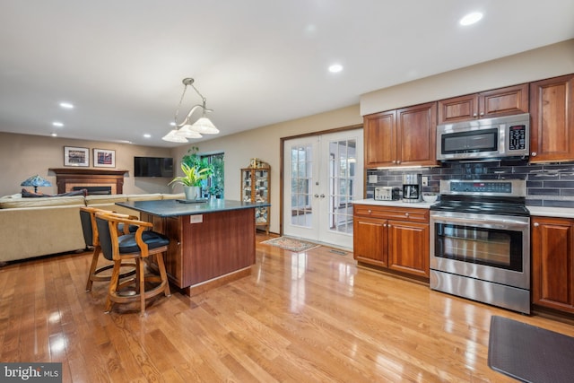 kitchen with a center island, hanging light fixtures, light wood-type flooring, appliances with stainless steel finishes, and a kitchen bar