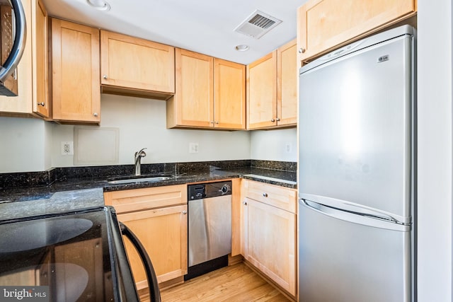 kitchen featuring light brown cabinetry, dark stone countertops, sink, and stainless steel appliances