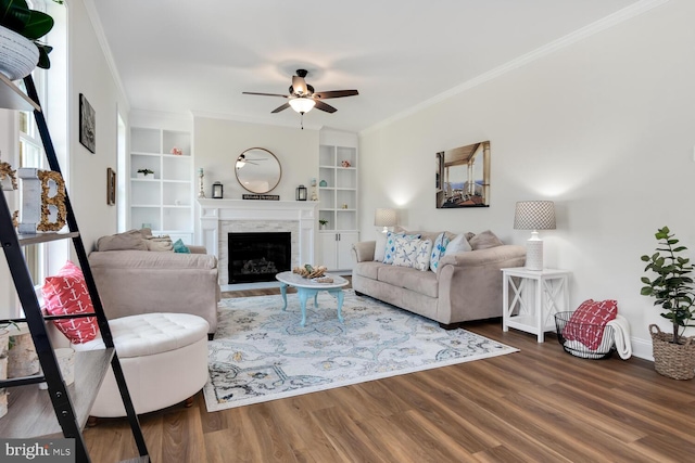 living room with built in shelves, ceiling fan, wood-type flooring, and crown molding