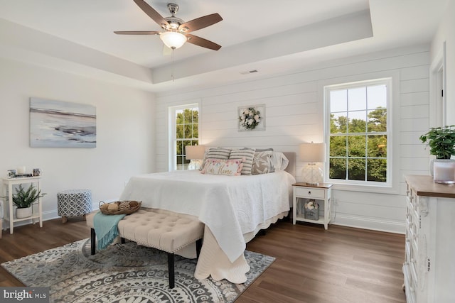 bedroom with a raised ceiling, dark hardwood / wood-style floors, and ceiling fan