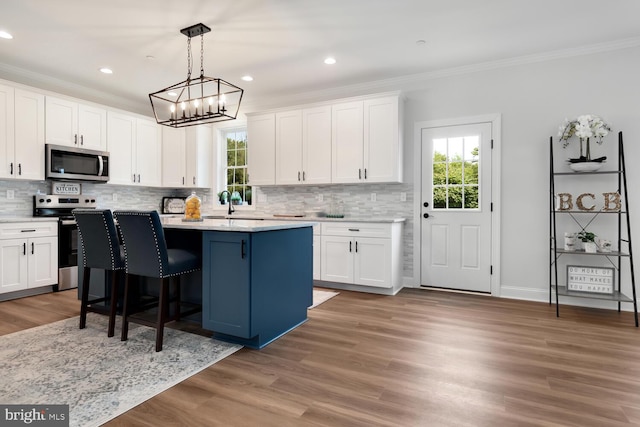 kitchen featuring a kitchen island, hardwood / wood-style floors, white cabinets, hanging light fixtures, and stainless steel appliances