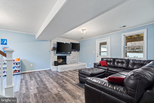 living room with a textured ceiling, wood-type flooring, ornamental molding, and a brick fireplace