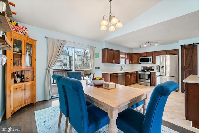 dining room featuring sink, a barn door, a chandelier, lofted ceiling, and light hardwood / wood-style floors