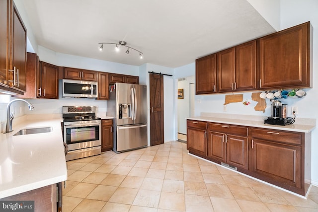 kitchen featuring sink, a barn door, appliances with stainless steel finishes, a baseboard radiator, and light tile patterned flooring