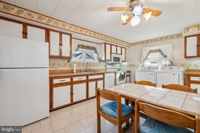 kitchen with sink, tile countertops, white appliances, white cabinets, and washer and dryer