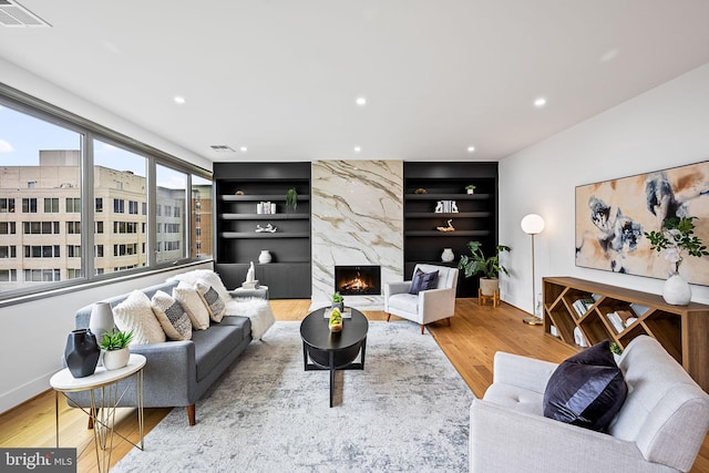 living room featuring built in shelves, light hardwood / wood-style floors, and a high end fireplace