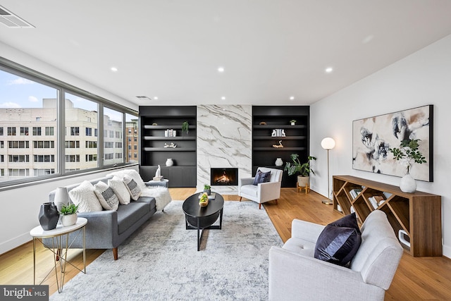 living room featuring light hardwood / wood-style floors, built in features, and a premium fireplace