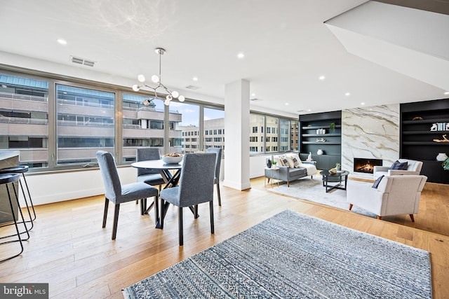 dining area featuring built in shelves, a high end fireplace, light hardwood / wood-style floors, and a notable chandelier