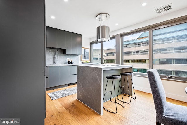 kitchen featuring a center island with sink, sink, hanging light fixtures, light wood-type flooring, and a breakfast bar area