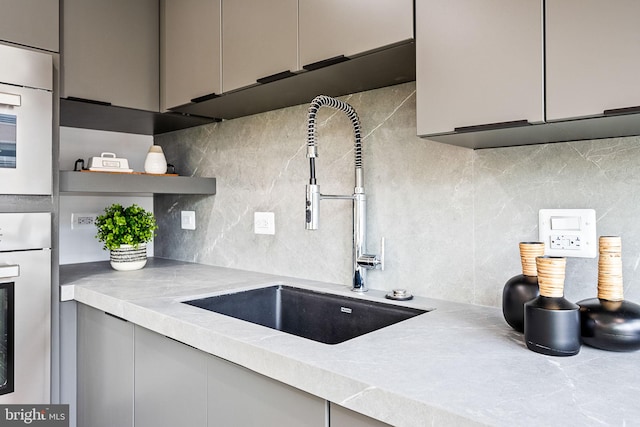 kitchen featuring tasteful backsplash, gray cabinetry, sink, and wall oven