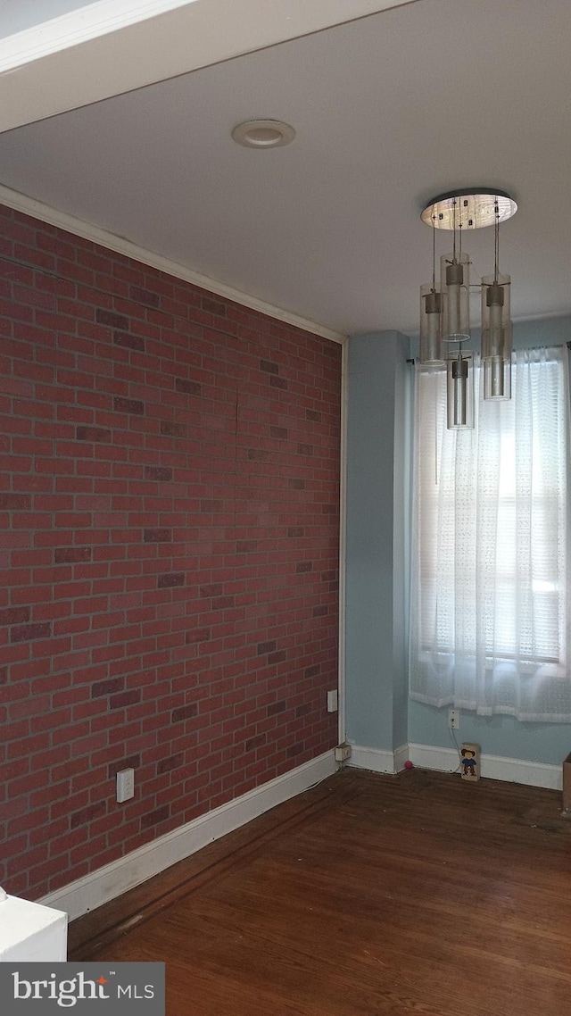 unfurnished dining area with dark hardwood / wood-style flooring, a notable chandelier, ornamental molding, and brick wall