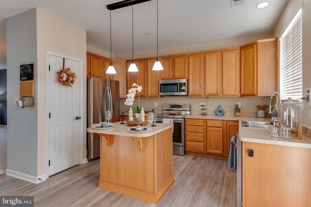 kitchen with sink, appliances with stainless steel finishes, light hardwood / wood-style floors, a kitchen island, and decorative light fixtures