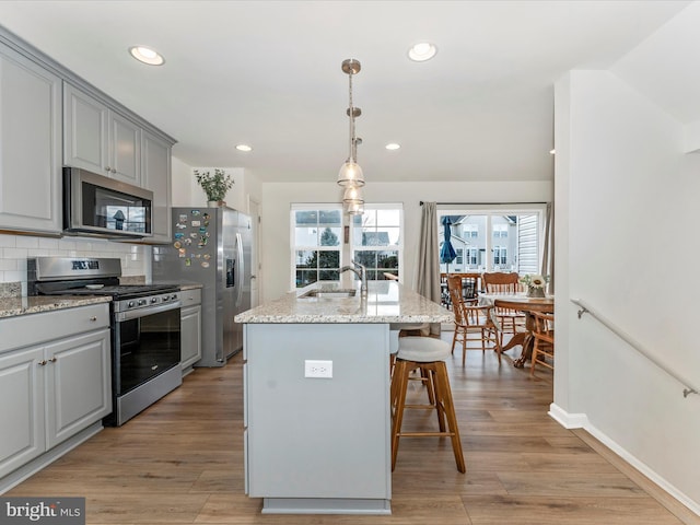 kitchen featuring sink, light stone counters, gray cabinets, a kitchen island with sink, and appliances with stainless steel finishes