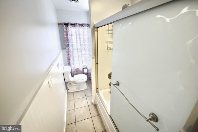 bathroom with tile patterned floors, toilet, and bath / shower combo with glass door