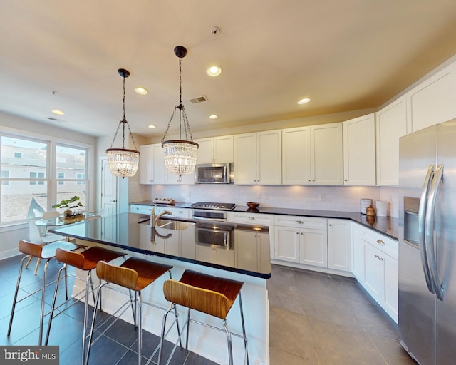 kitchen featuring decorative light fixtures, a kitchen island with sink, appliances with stainless steel finishes, white cabinets, and a chandelier