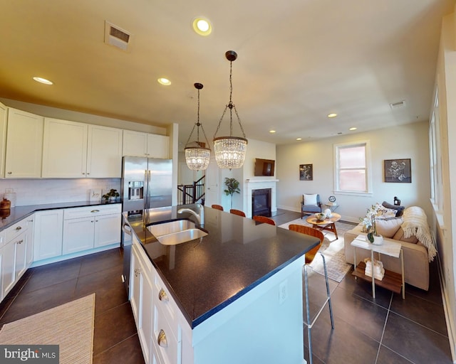 kitchen featuring sink, hanging light fixtures, a kitchen island with sink, stainless steel fridge with ice dispenser, and white cabinets