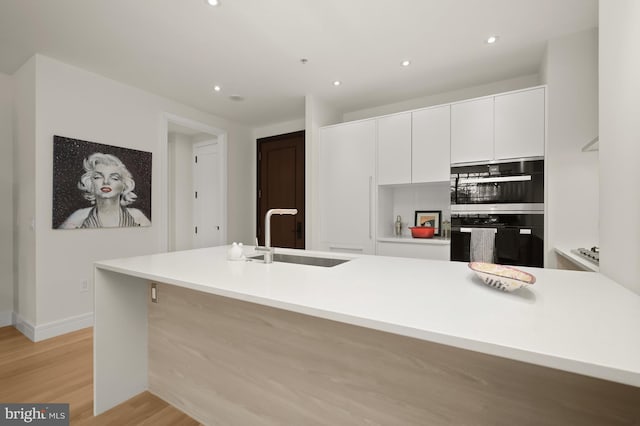 kitchen featuring white cabinets, a center island with sink, light hardwood / wood-style flooring, and sink