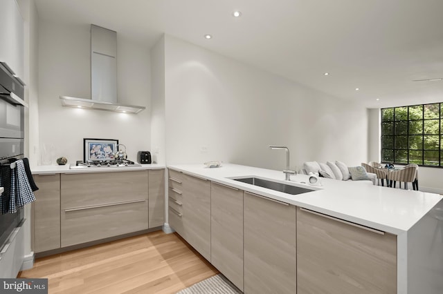 kitchen featuring sink, wall chimney exhaust hood, light hardwood / wood-style floors, kitchen peninsula, and stainless steel gas cooktop