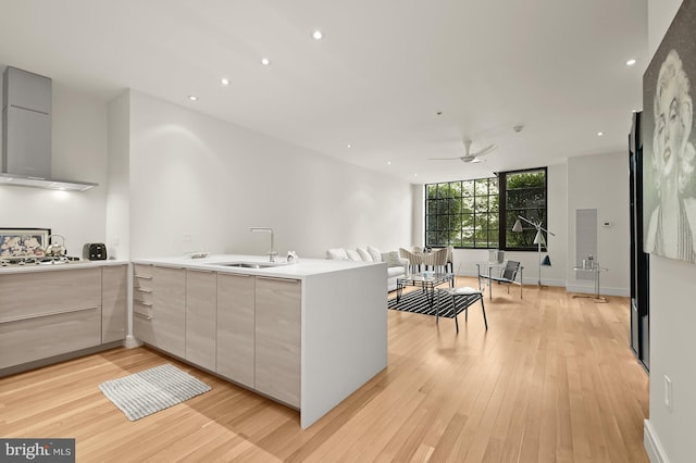 kitchen with sink, wall chimney range hood, stainless steel gas cooktop, light hardwood / wood-style flooring, and kitchen peninsula