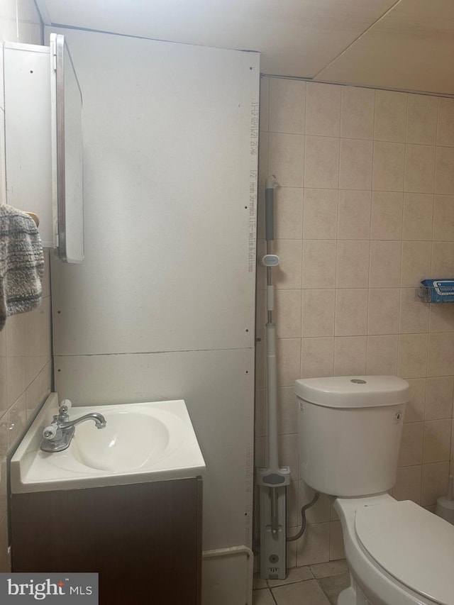 bathroom featuring toilet, vanity, tile patterned floors, and tile walls