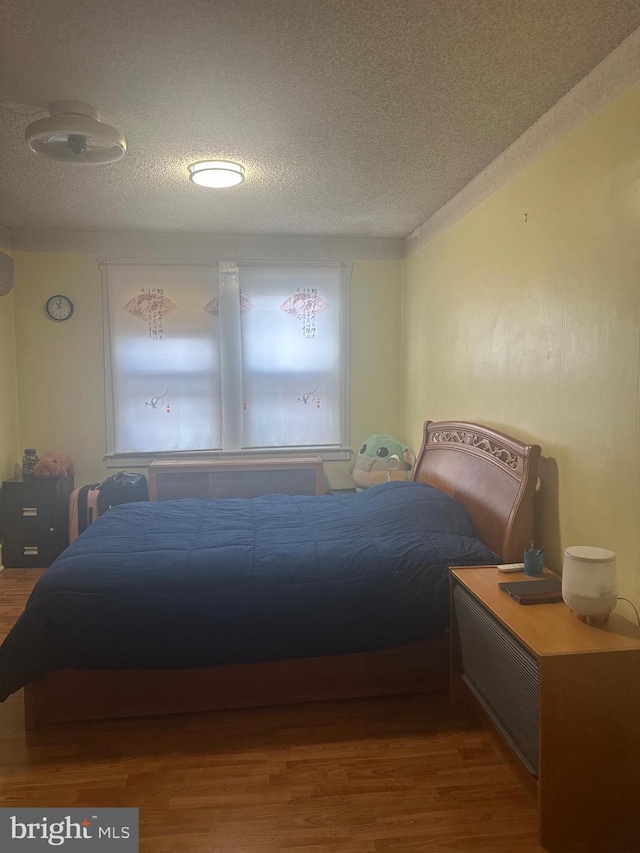 bedroom with wood-type flooring, a textured ceiling, and radiator