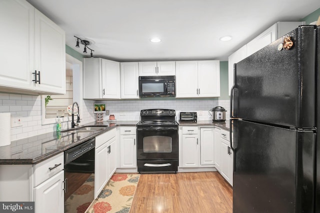 kitchen featuring black appliances, white cabinets, sink, dark stone countertops, and light wood-type flooring