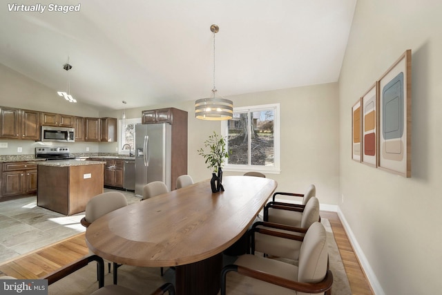 dining room with sink, lofted ceiling, light hardwood / wood-style flooring, and a chandelier