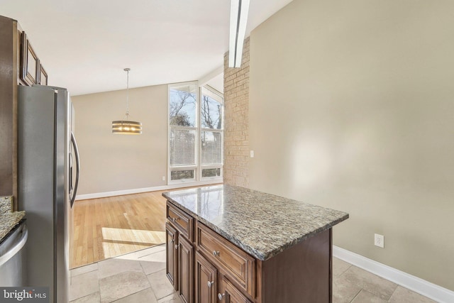 kitchen featuring a center island, decorative light fixtures, vaulted ceiling, stone countertops, and stainless steel refrigerator