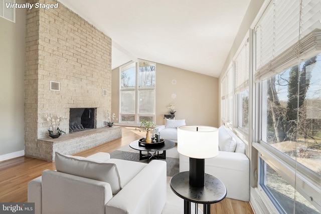 living room featuring a brick fireplace, light hardwood / wood-style floors, and vaulted ceiling