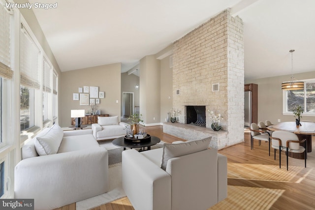 living room with light hardwood / wood-style flooring, high vaulted ceiling, a notable chandelier, and a brick fireplace