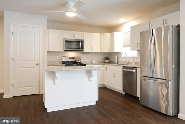 kitchen featuring a center island, white cabinets, dark hardwood / wood-style floors, appliances with stainless steel finishes, and a kitchen bar