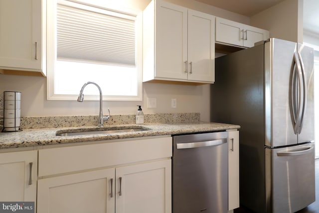 kitchen with white cabinets, stainless steel appliances, light stone counters, and sink