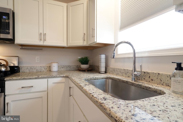 kitchen with white cabinetry, light stone counters, black / electric stove, and sink