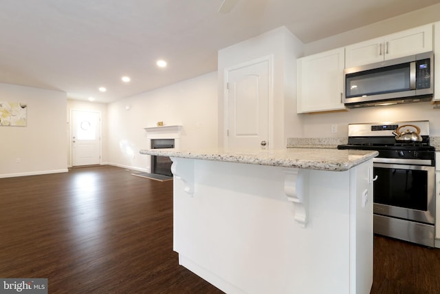 kitchen featuring dark hardwood / wood-style flooring, light stone counters, stainless steel appliances, white cabinets, and a center island