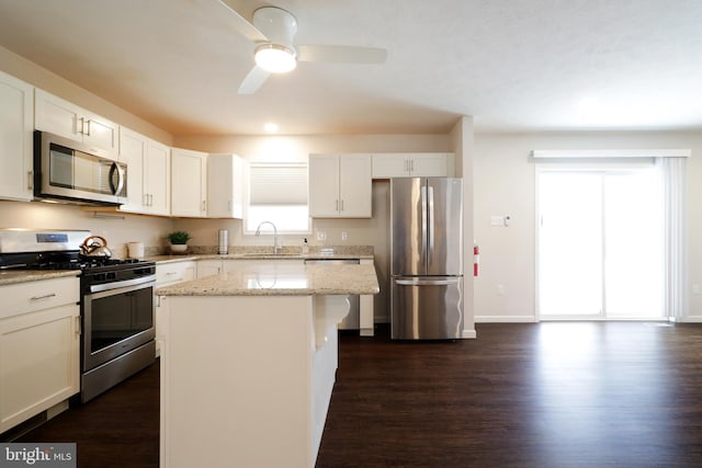 kitchen featuring light stone counters, stainless steel appliances, sink, a center island, and white cabinetry