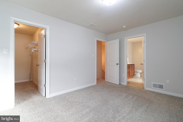 unfurnished bedroom featuring ensuite bathroom, light colored carpet, a spacious closet, and a closet