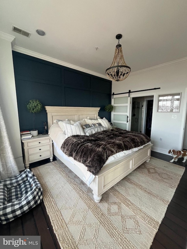 bedroom with a barn door, crown molding, and hardwood / wood-style floors