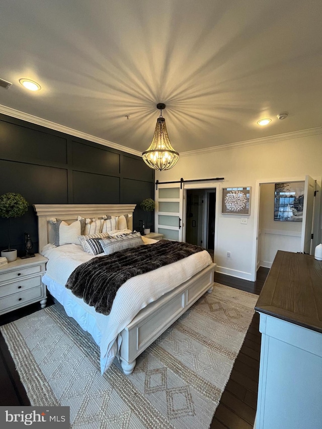 bedroom featuring a barn door, hardwood / wood-style flooring, ornamental molding, and a notable chandelier