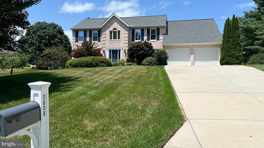 colonial-style house featuring brick siding, a garage, concrete driveway, and a front yard
