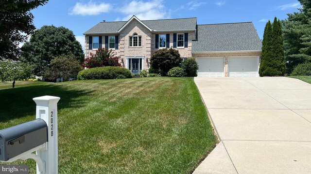 colonial-style house featuring brick siding, a garage, concrete driveway, and a front yard