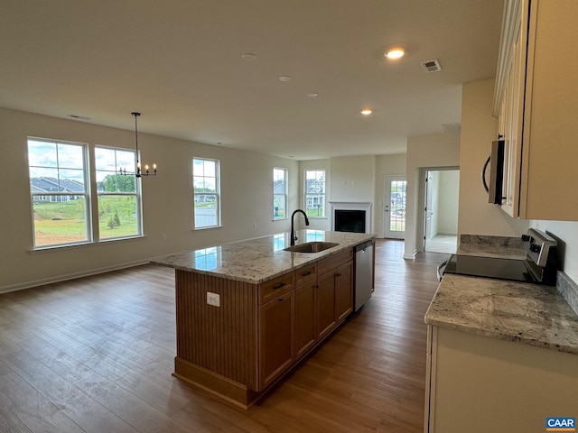 kitchen with sink, light wood-type flooring, an island with sink, appliances with stainless steel finishes, and decorative light fixtures