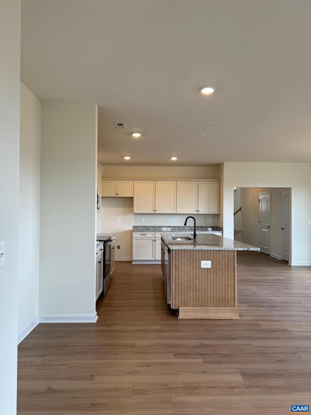 kitchen with light stone countertops, sink, stainless steel appliances, light hardwood / wood-style floors, and a center island with sink