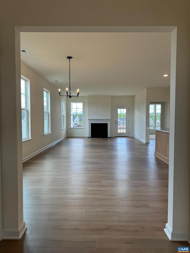 unfurnished living room featuring a healthy amount of sunlight, light hardwood / wood-style floors, and an inviting chandelier