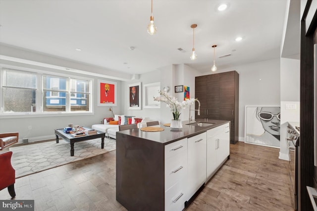 kitchen featuring hardwood / wood-style floors, white cabinets, a center island with sink, sink, and hanging light fixtures