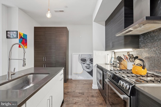 kitchen with dark hardwood / wood-style flooring, stainless steel gas range, wall chimney range hood, sink, and decorative light fixtures