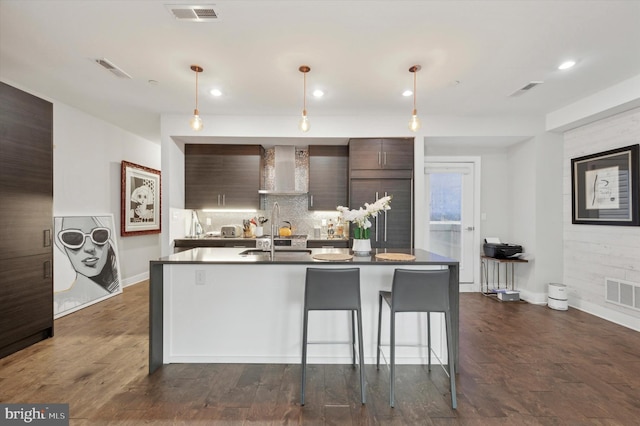 kitchen featuring wall chimney exhaust hood, decorative light fixtures, dark brown cabinets, and backsplash