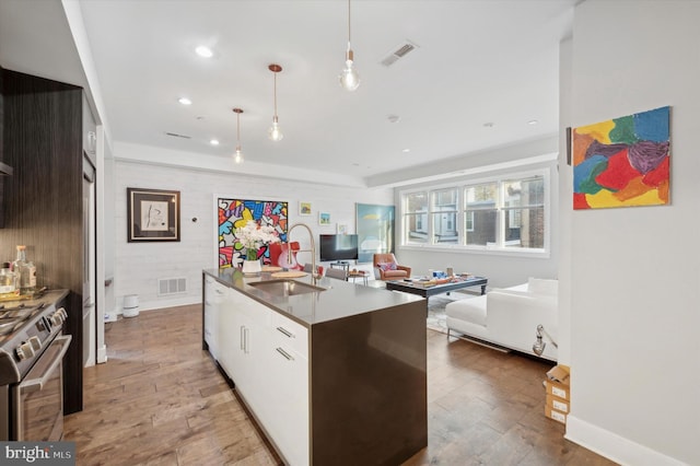 kitchen featuring stainless steel range, a kitchen island with sink, sink, pendant lighting, and hardwood / wood-style flooring